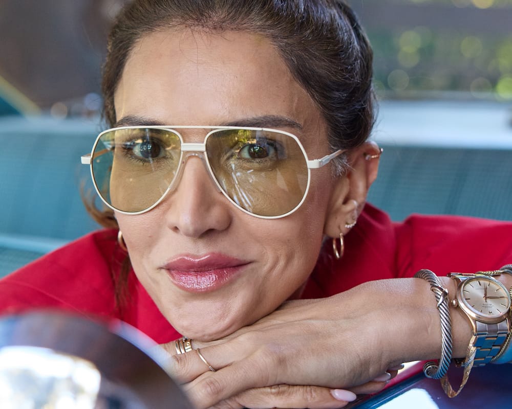 Woman wearing white aviator glasses and a red top, with a blurred background